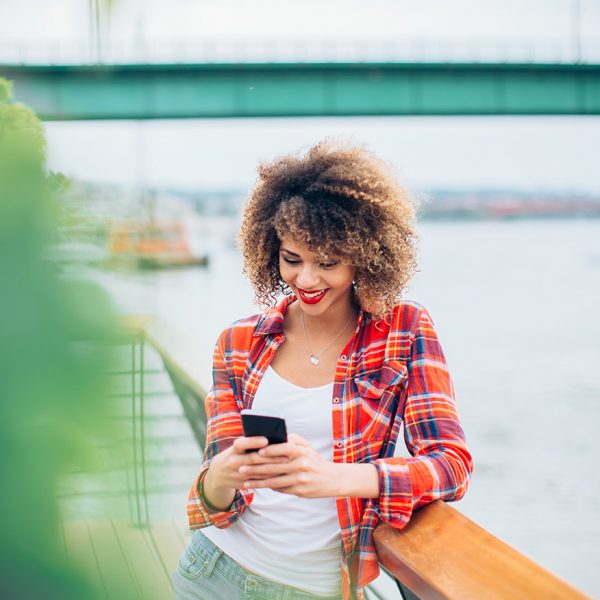 Young woman standing at the balcony and using mobile phone