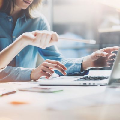 Image of someone working on a laptop and another pointing at the screen with a pencil.